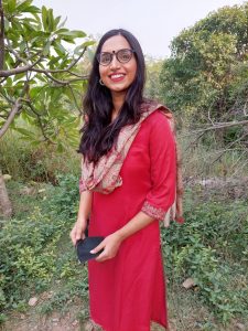 Shreyasi smiling at the camera in a red dress amidst greenery