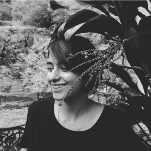 A black and white photo of Rohini, smiling away from the camera with some foliage covering the right side of her face.